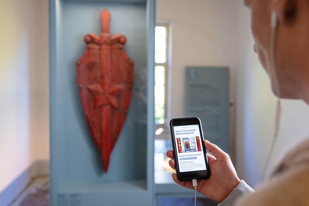 [Translate to English:] Audioguide-Station am einem Emblem des KGB in der Daueruausstelllung.